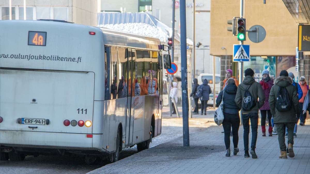 Linja-auto on pysähtynyt pysäkille, ja ihmisiä kävelee kadulla Oulun keskustassa.