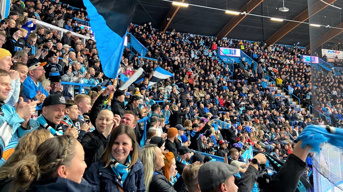 Ihmiset iloitsevat täydessä jääkiekkokatsomossa. Lähikuva Pelicans-faneista. Ihmset heiluttavat lippuja. 