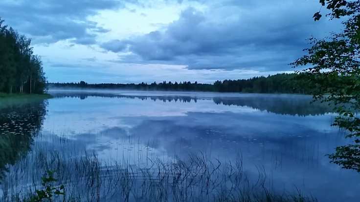 Sininen hetki kylmänä juhannuksena Juvalla vuonna 2014, pilvet roikkuvat matalalla peilityynen järven yllä.