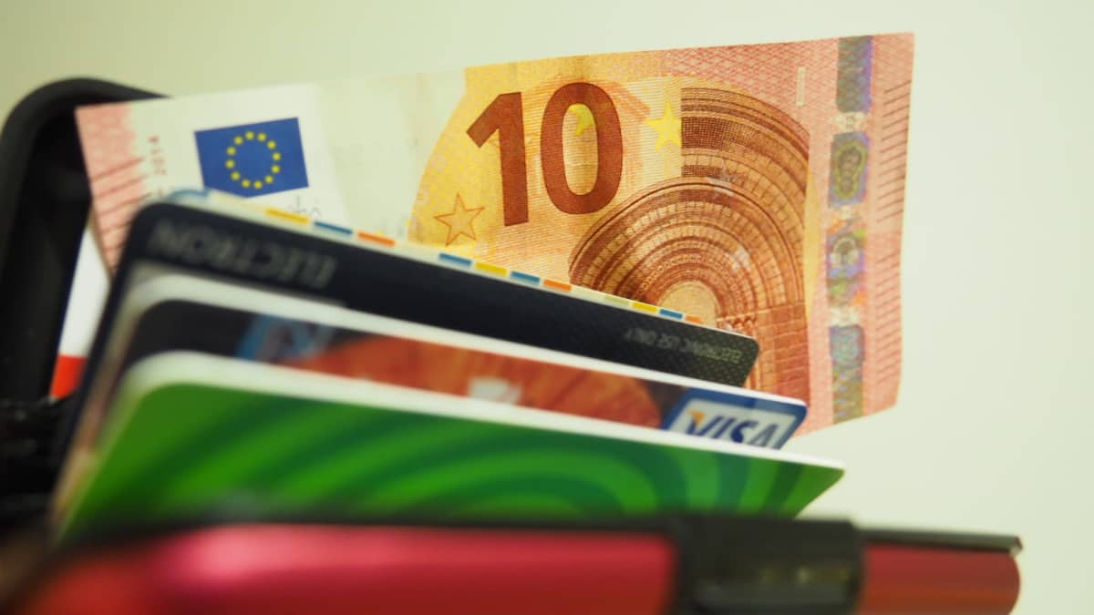 Kymmenen euron seteli pilkistää lompakosta korttien joukosta.