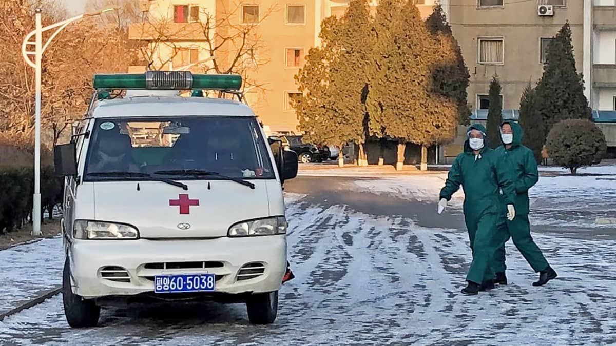 Ambulanssi ja ihmisiä suojavarusteissa Pjongjangissa