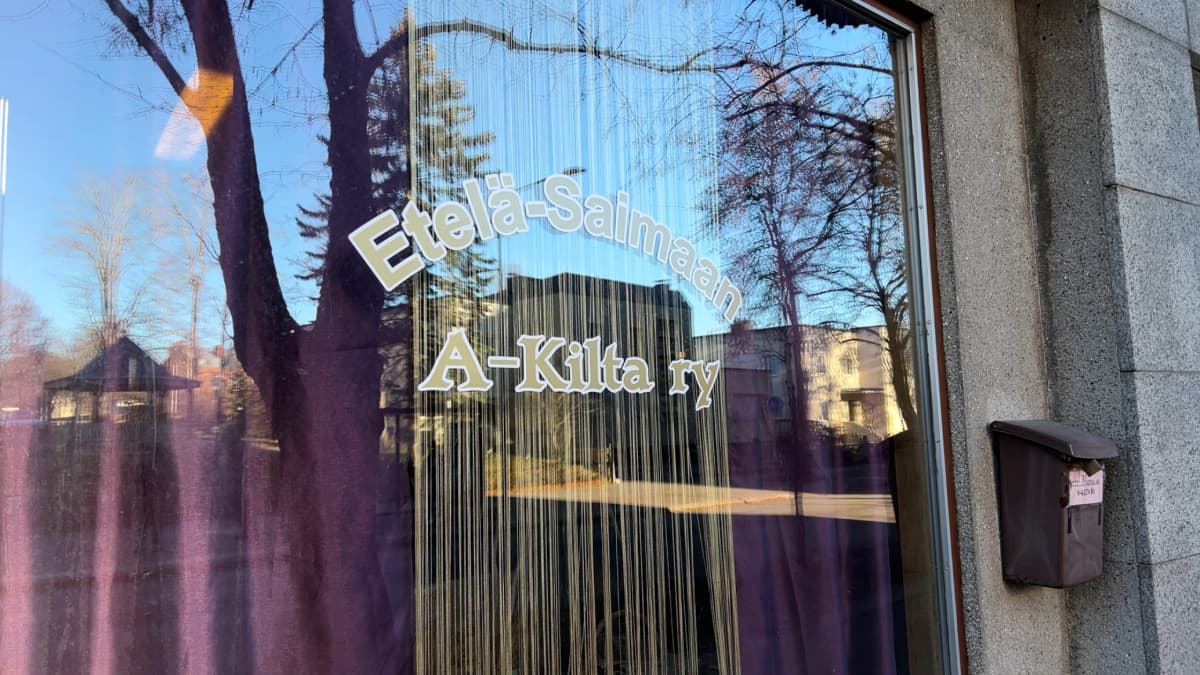 Ikkunassa lukee teksti: Etelä-Saimaan A-Kilta ry. Ikkunassa on violetit verhot ja seinällä on postilaatikko.