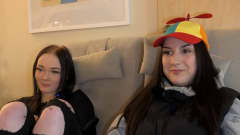 Kaksi tyttöä istuu sohvalla. Toisella on värikäs lippis päässä.