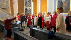 Punaisiin vaatteisiin pukeutuneet naiset laulavat kirkossa, alttarin edustalla
