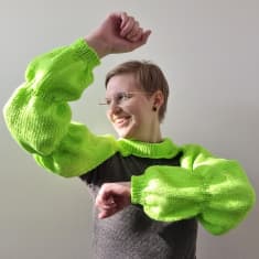 Käsityöharrastaja Sanna Pyykönen on pukeutunut neulomaansa kirkaanvihreään boleroon, joka muistuttaa Käärijän hihoja.
