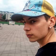 Nuori turkulaisartisti Louie Blue katsoo kameraan, taustalla Turun jokirantaa.