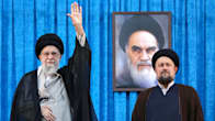 Ali Khamenei ja Hassan Khomeini seisovat sinisen verhon edessä. Khamenei nostaa kättään tervehdykseen. Taustalla on ajatolla Ruhollah Khomeinin kuva.