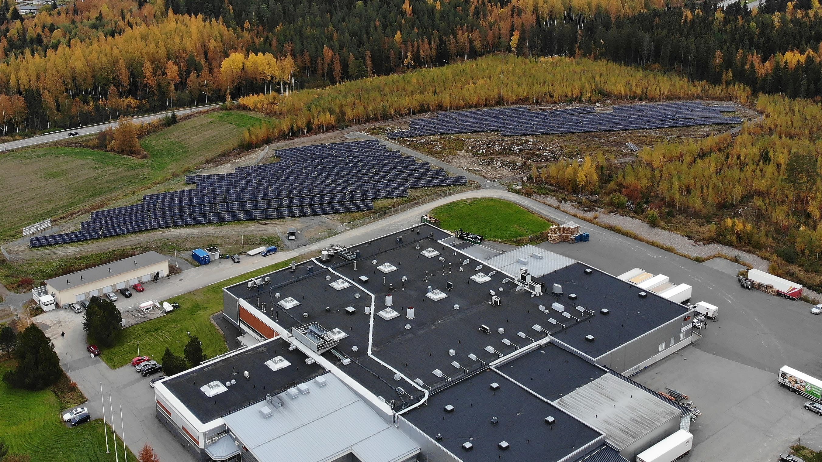 Ilmakuvassa etualalla tuotantolaitos ja sen takana kenttä, jossa on tuhansia aurinkopaneeleita.