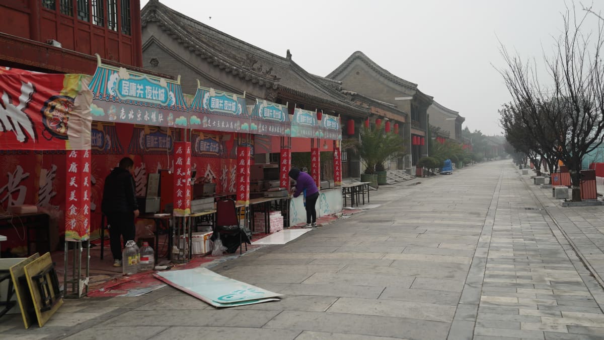 kiinalaisia punaisia kaarevakattoisia rakennuksia tien laidassa ja etualalla kauppa jota korjataan
