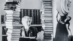Agatha Christie katsoo kameraan kahden korkean kirjapinon välistä.