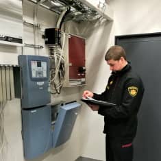 Palotarkastaja MIka Kinnunen tarkastaa sisätiloissa seinällä olevia sähkölaitteita.