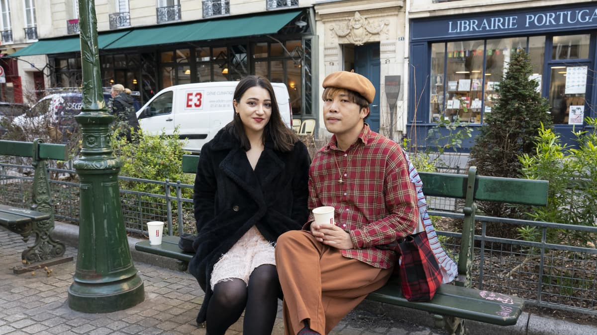 Nuori nainen ja mies istuvat vihreällä penkillä Pariisissa.