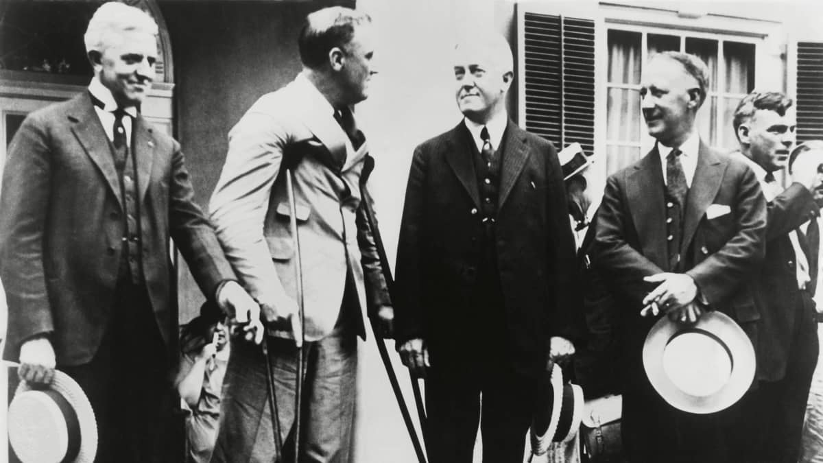  Franklin Roosevelt seisoo keppien varassa ja keskustelee tummapukuisten ihmisten kanssa.