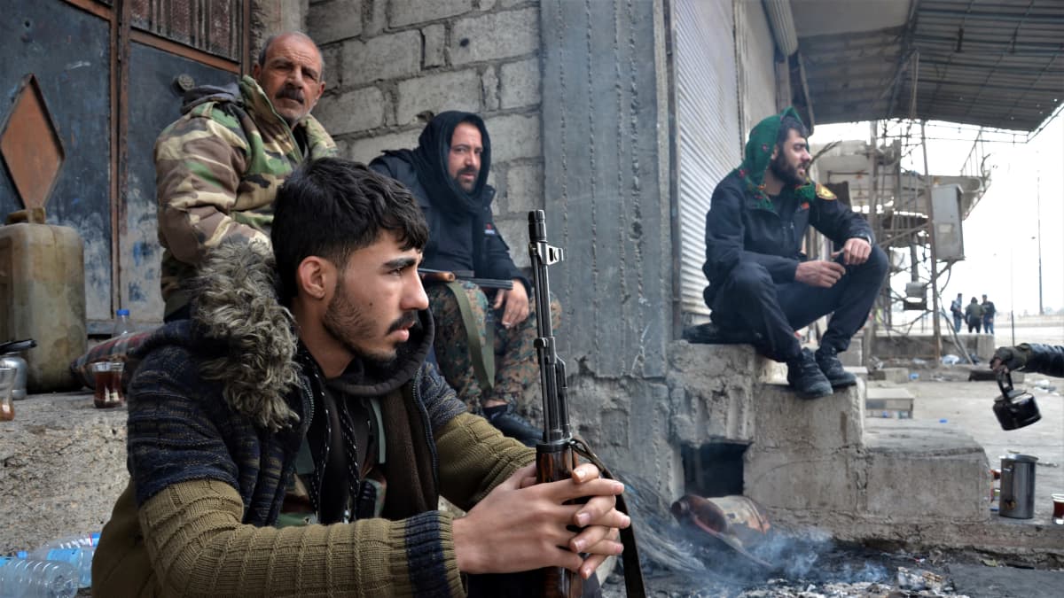 Syyrialaisia taistelijoita istumassa rakennuksen edustalla.