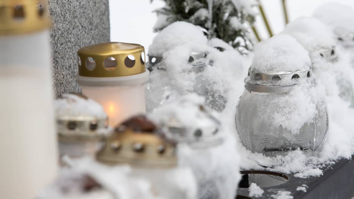 Hautakynttilöitä lumisessa maisemassa hautausmaalla