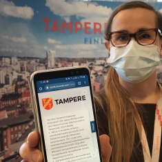 Nainen näyttää matkapuhelimesta koronabottisovellusta