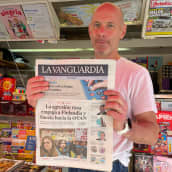 Barcelonalainen lehtimyyjä näyttää kameralle paikallisen sanomalehden kantta, jossa otsikoissa Suomea koskeva uutinen. 