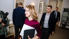Pitkätukkainen nainen lyhythihaisessa mekossa saapuu kokoukseen avustajien ja kuvaajien ympäröimänä.