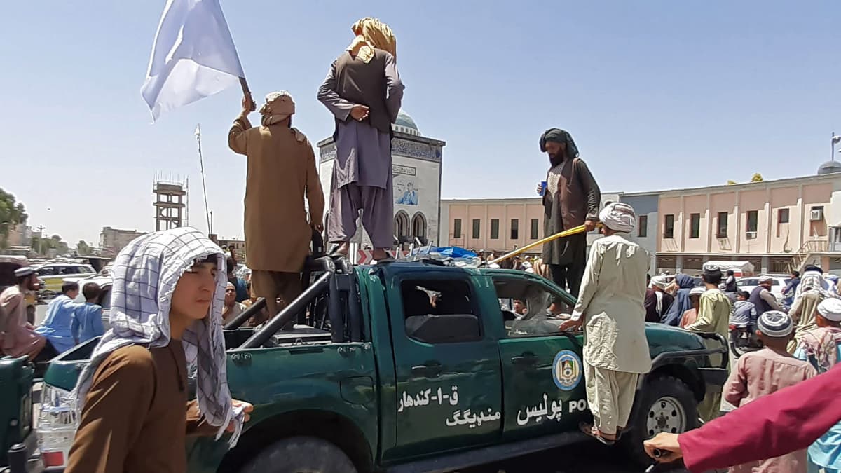 Taliban-taistelijat seisovat vaurioituneen poliisiauton päällä.