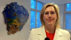 Työministeri Tuula Haatainen seisoo villasukista tehdyn taideteoksen edessä.
