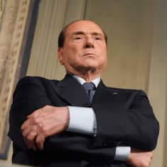 Silvio Berlusconi vakavailmeisenä kädet puuskassa.