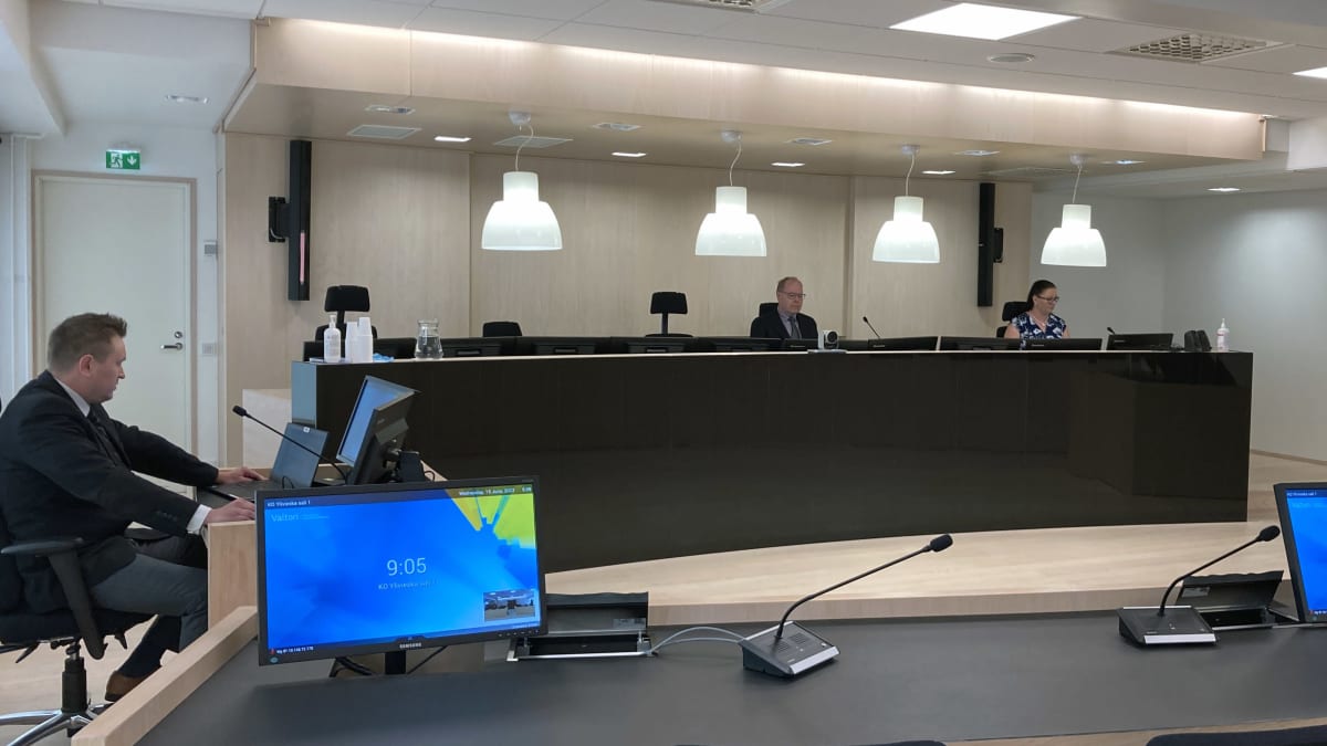 Oikeudenistunto, jossa vasemmalla istumassa mies ja takana päydän takana mies ja nainen.