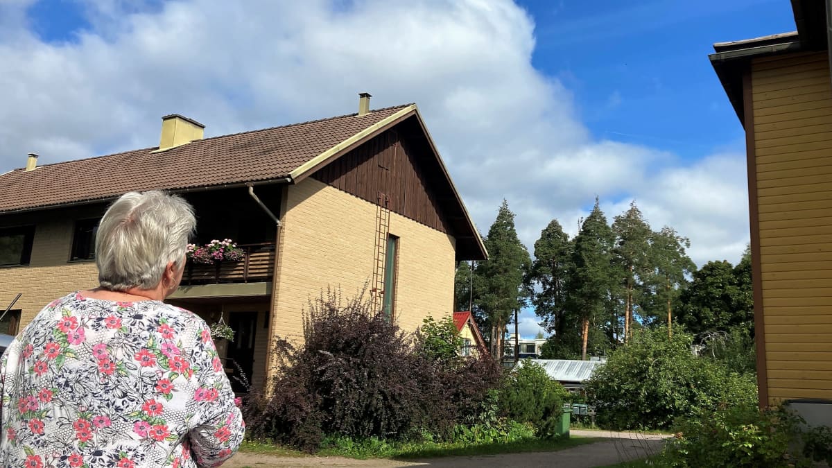 Päivi Leskinen-Kilkki katsoo talojen välistä taivaalle, jossa näkyy häivähdys lentokoneen jättämää valkeaa vanaa.