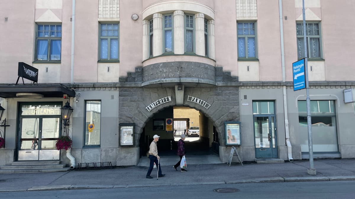 Kaksi ihmistä kävelee vanhan kivitalon porttikongin ohi Tampereen keskustassa. 