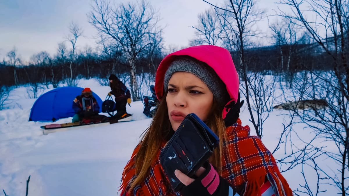 Hilda Länsman pitää puhelinta kädessään Inarin disko -kuvauksista lumisessa maisemassa. Taustalla näkyy sininen teltta ja kaksi ihmistä.