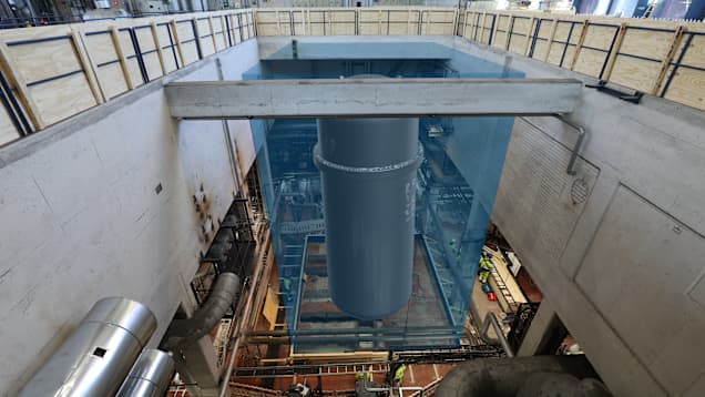 Kuva laitoksen hallista, johon on tietokoneella lisätty vesiallas ja harmaa lieriön muotoinen reaktori. 