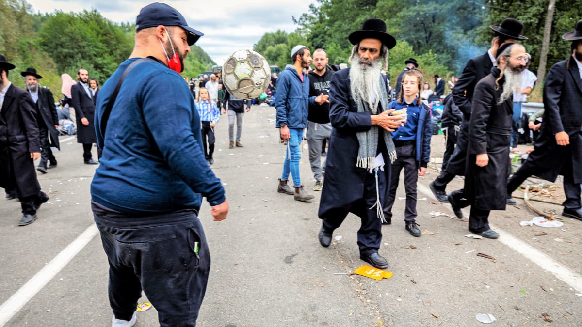 Mies potkii jalkapalloa tiellä. Ohi kulkevat perinteisiin asuihin pukeutuneet hasidijuutalainen katsoo häntä. Tiellä on muutenkin paljon väkeä.