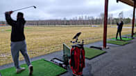 Två personer tränar golfslag på en driving range under tak.