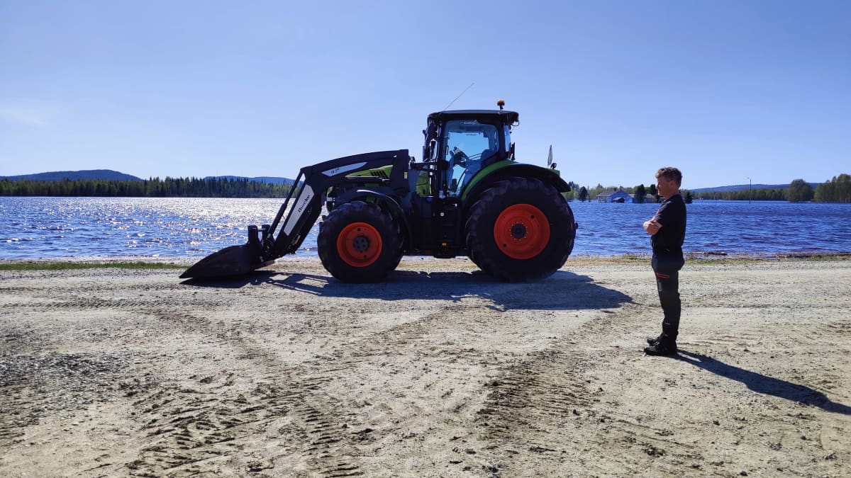 Mies seisoo traktorin vieressä. Taustalla näkyy veden valtaama pelto.