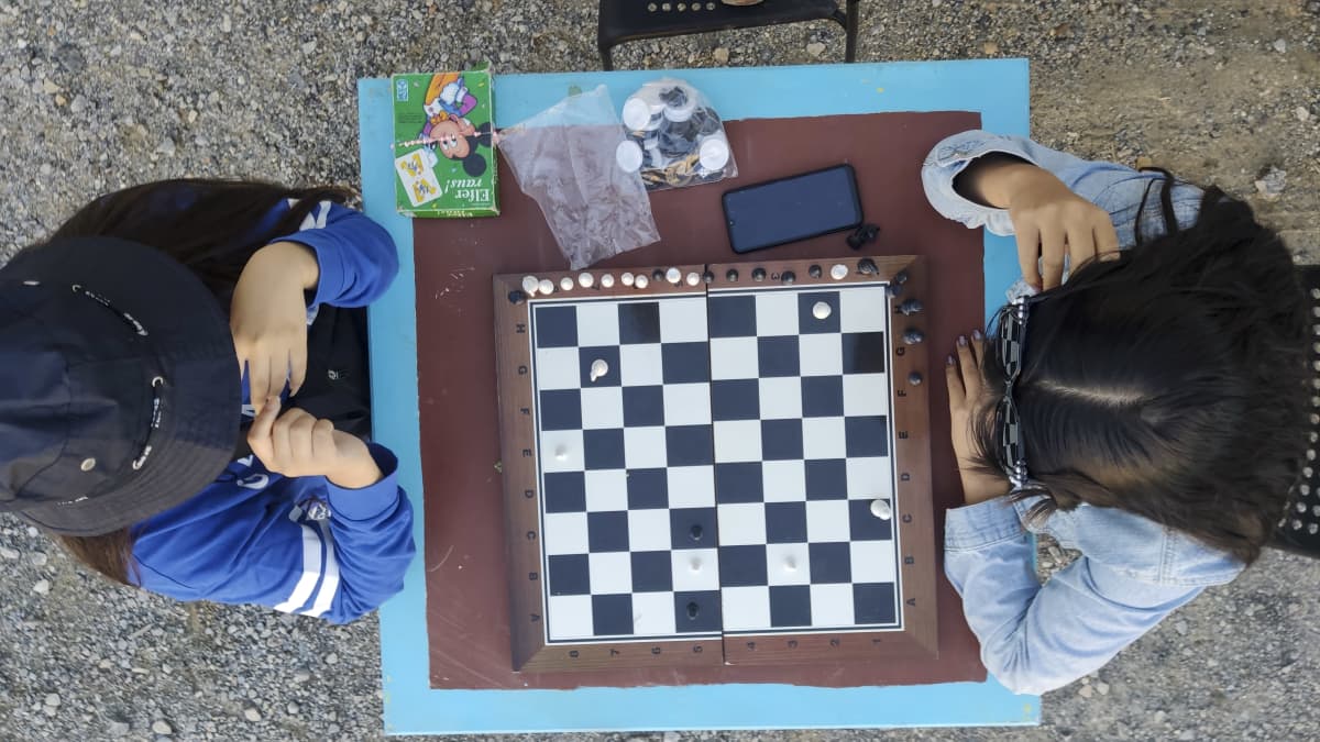 Kaksi lasta pelaa shakkia vastaanottokeskuksessa. Kuvassa näkyy pelilauta.