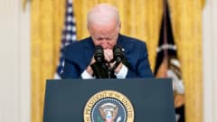 Joe Biden nojaa käsiään puhujanpönttöön ja leukaansa ristissä oleviin käsiinsä. Taustalla näkyy Yhdysvaltain lippu.