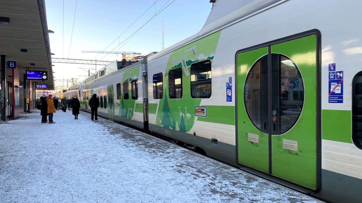 Lahden rautatieasemalla VR:n juna laiturilla pysähtyneenä, matkustajat kävelevät kohti junan sisäänkäyntejä. Talvi, lunta laiturilla.