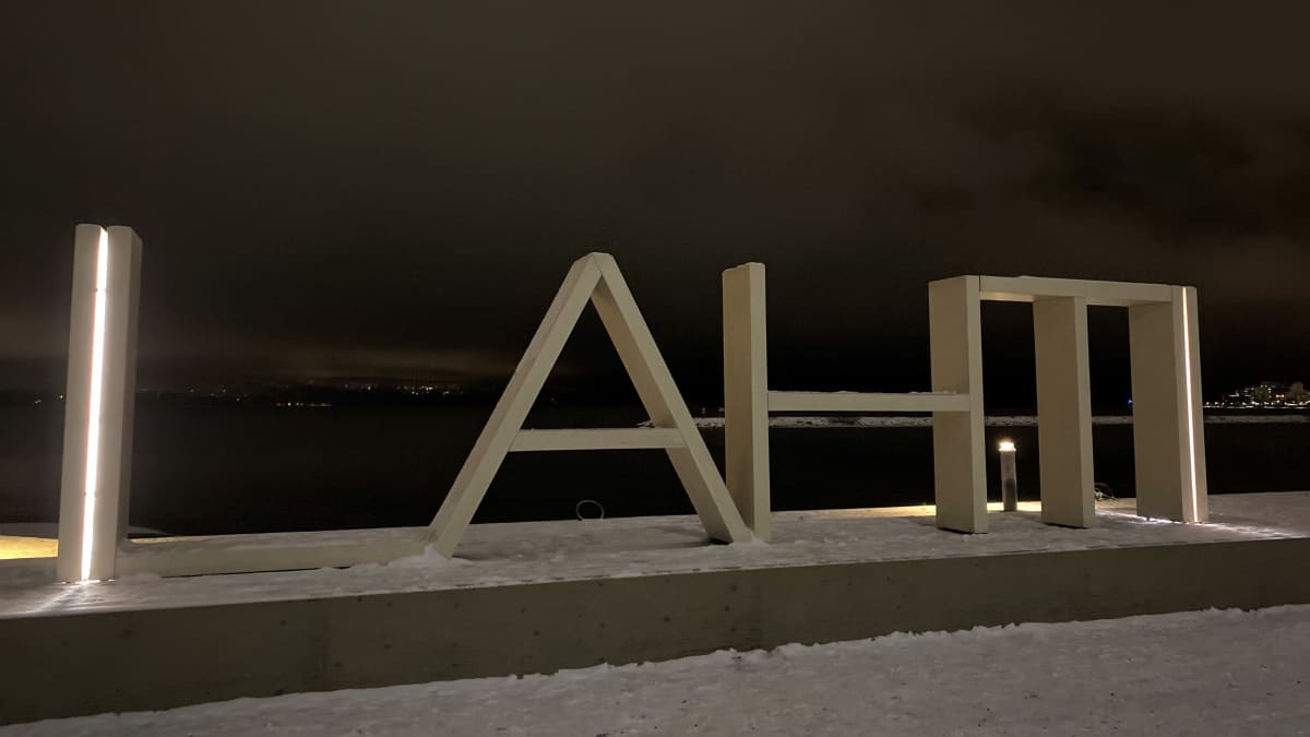 Puinen kirjainlogoteos seisoo talvisen järven rannassa. Logon teksti on Lahti. 