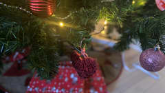 Joulukuusen koristeita, palloja ja sydän ja kuusen alla on lahjoja.