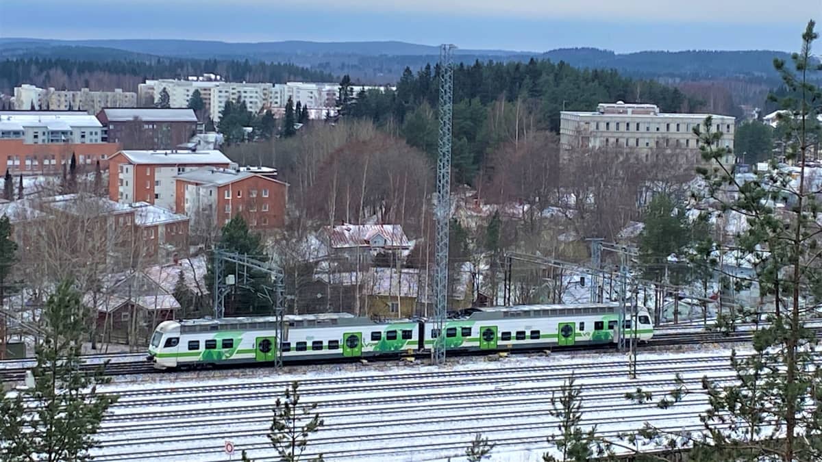 VR:n vihreävalkoinen juna ajaa raiteilla. Lunta maassa, ympärillä puita ja kerrostaloja Lahdessa.