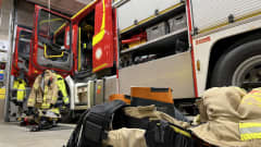 Palolaitoksen auto sisällä hallissa, sen vieressä palomiesten varusteita valmiina hälytystä varten.