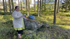 Katja Manninen pitää kädessään kuppia ja katsoo sivuun kamerasta, taustalla metsää ja sairaalarakennuksia