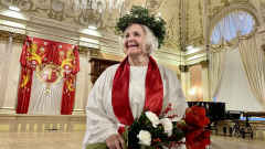 Vaasan Lucia-mummo 2022 seisoo juhlasalissa kynttiläkruunu päässään ja kukkakimppu käsissään.
