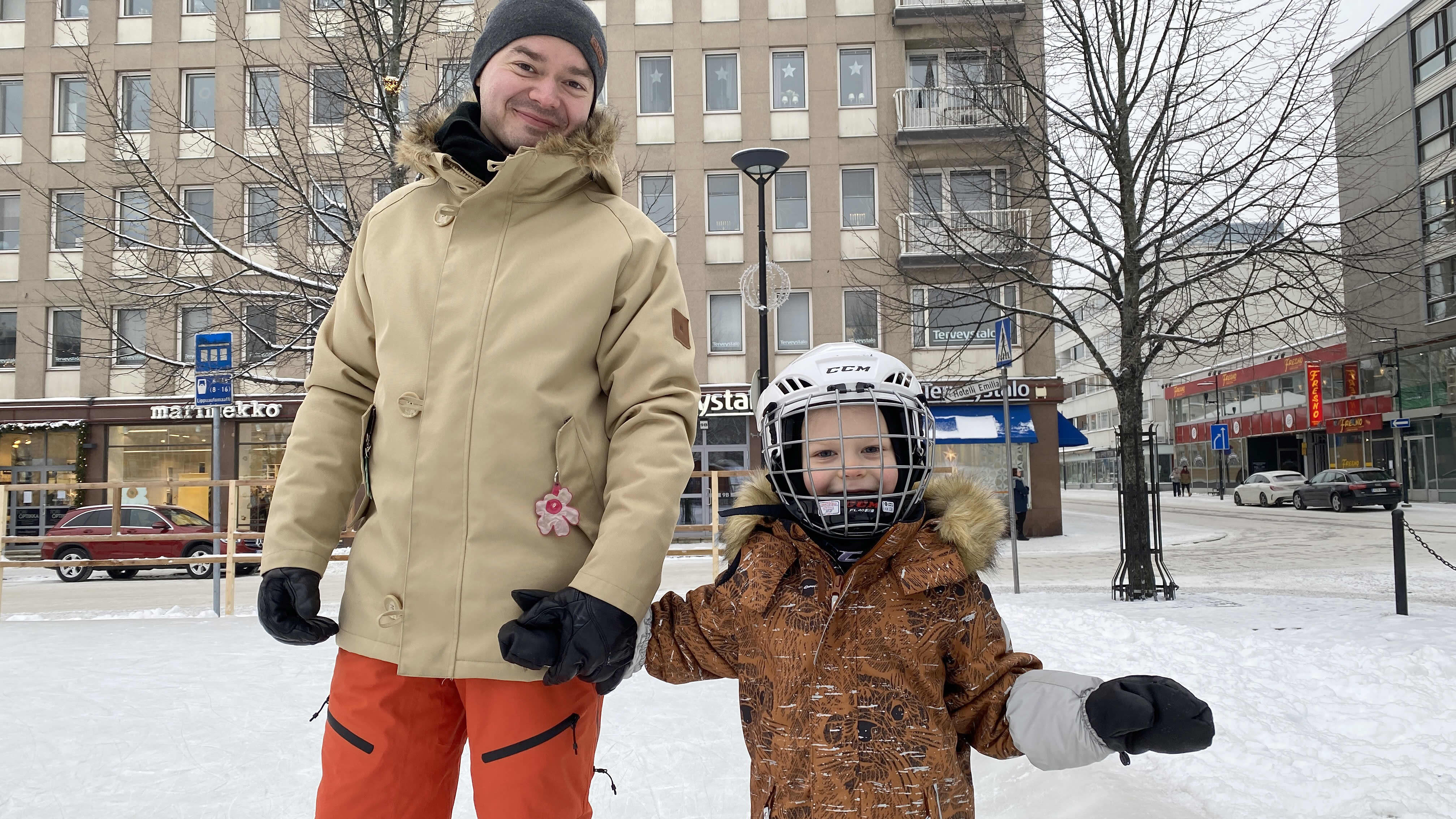 Isä Aleksi Aromaa ja poika Okko Aromaa luistelemassa Hämeenlinnan torin jäällä käsi kädessä, hymyilevät kameralle.