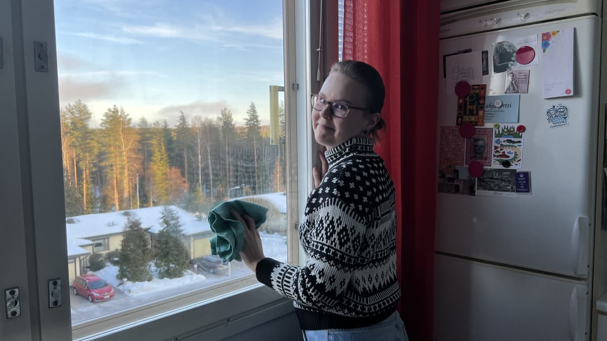 Nainen pyyhkii rätillä keittiön ikkunaa.