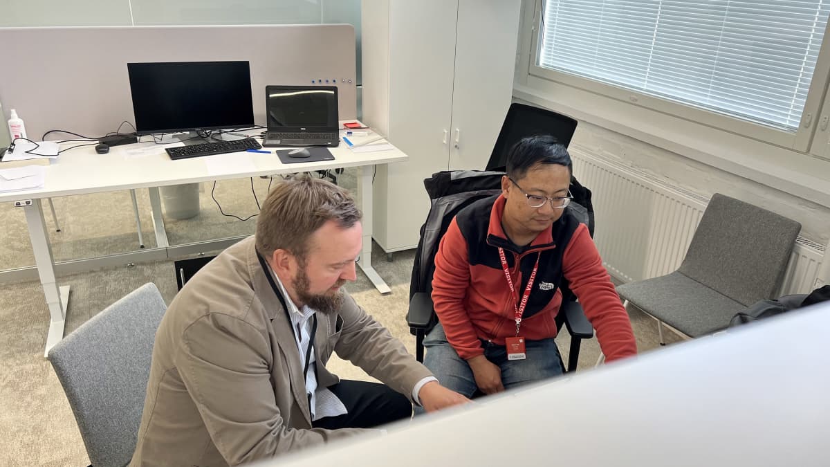 Sähköisen liikenteen professori Lassi Aarniovuori ja professori Dong Liu työhuoneessa tietokoneen äärellä. Istuvat vierekkäin ja katsovat koneen näyttöön, kuva edestä ylhäältä.