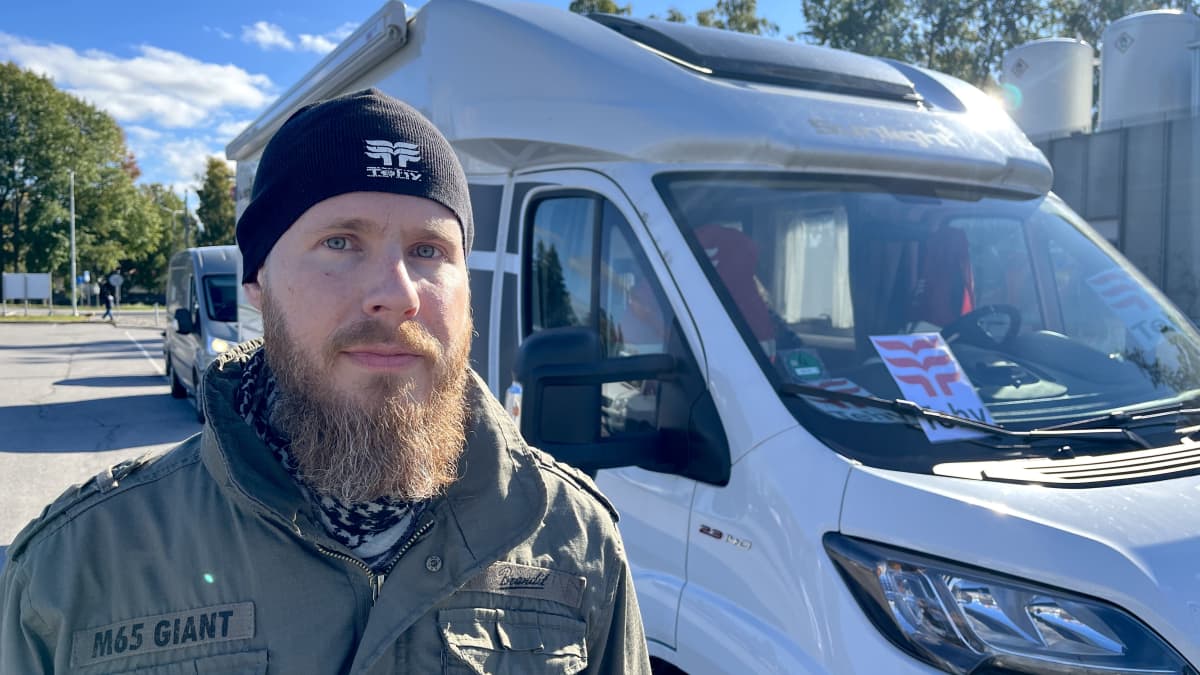 Tehyn pääluottamusmies Atte Tahvola seisoo pakettiauton edessä. Päässään musta pipo, ruskea pitkähtö parta, vihreä armeijatyylinen takki päällään. Katsoo vakavana kuvaajaa. 