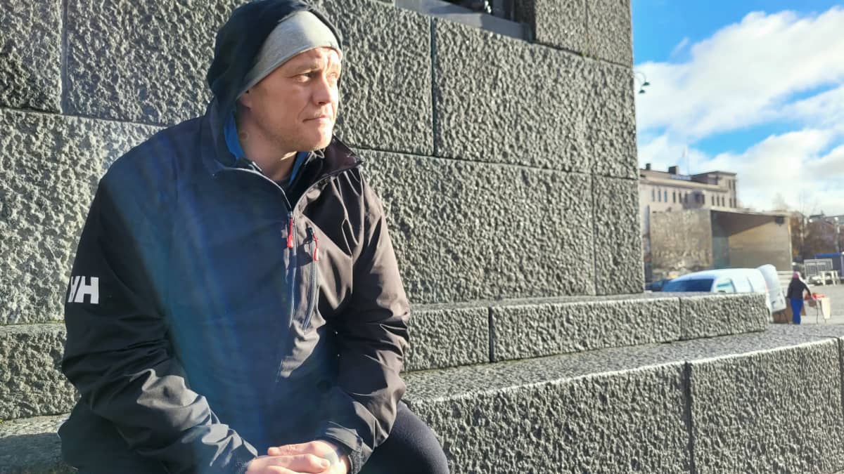 Tomi Bäckman istuu ulkona kiviseinän vieressä.