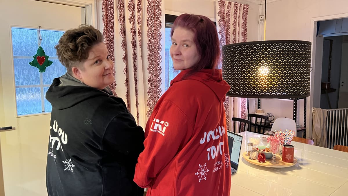 Kaksi naista seisoo keittiönpöydän äärellä. Vasemmanpuoleisella Sari Mämmiojalla on musta huppari, jossa näkyy osittain tekstiä jouluapu. Oikeanpuoleisella Maria Kallungilla on punainen huppari, jossa näkyy tekstiä jouluapu.