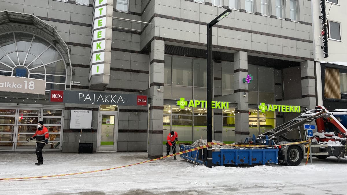 Kaksi huoltoyhtiön työntekijää siivoaa romahtaneen kattorakenteen roskia kadulta roskalavalle.