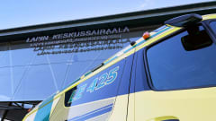 Vihreäkeltainen ambulanssin Lapin keskussairaalan edustalla. Taustalla sairaalan kyltti lasiseinällä.
